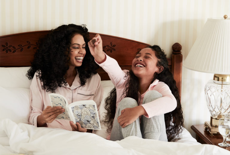 Mother and daughter reading book on a bed in a Little America Hotel guest room.